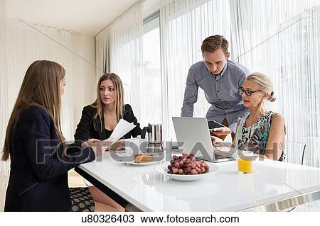 Stock Image - Colleagues at table having breakfast meeting looking at paperwork. Fotosearch