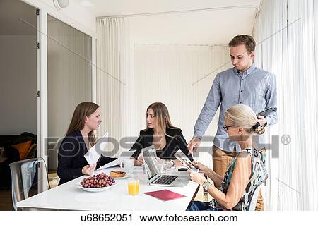 Colleagues sitting at table having business breakfast meeting holding digital tablet looking at photographs View Large Photo Image Stock Image - Colleagues sitting at table having business breakfast meeting holding digital tablet looking at photographs. Fotosearch