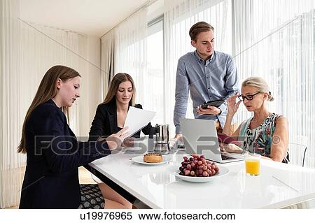 Colleagues sitting at table holding digital tablet and paperwork having business breakfast meeting View Large Photo Image Stock Photography - Colleagues sitting at table holding digital tablet and paperwork having business breakfast meeting. Fotosearch