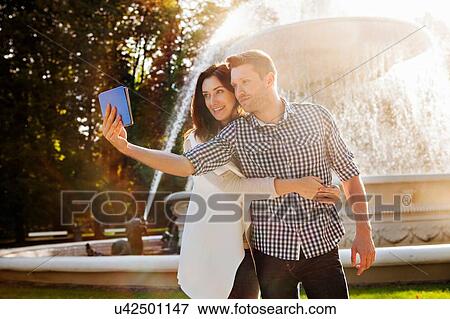 Couple taking selfie on digital tablet in park View Large Photo Image Stock Photo - Couple taking selfie on digital tablet in park. Fotosearch