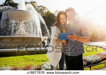 Couple using digital tablet in park View Large Photo Image Stock Photograph - Couple using digital tablet in park. Fotosearch