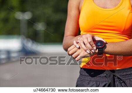 Stock Image - Cropped shot of young female runner setting smartwatch in parking lot. Fotosearch