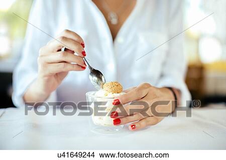 Picture - Cropped shot of young woman eating gelato with amaretti at table. Fotosearch