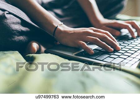 Cropped view of mid adult woman sitting cross legged on bed typing on laptop computer View Large Photo Image Stock Image - Cropped view of mid adult woman sitting cross legged on bed typing on laptop computer. Fotosearch