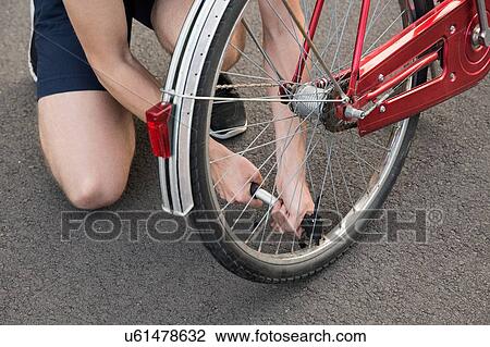 Stock Image - Cropped view of young man kneeling inflating bicycle tyre. Fotosearch