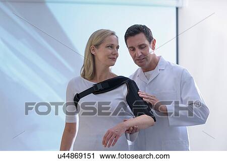 Stock Image - Doctor fitting orthopaedic sling to patient. Fotosearch
