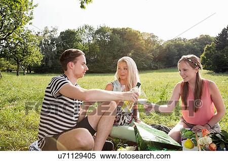Stock Photography - Family sitting on grass in park enjoying a glass of wine. Fotosearch