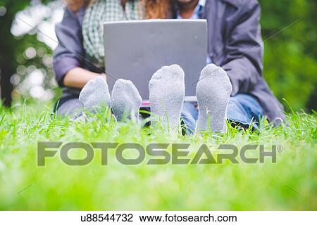 Stock Image - Feet of young couple wearing socks sitting on grass using laptop computer. Fotosearch