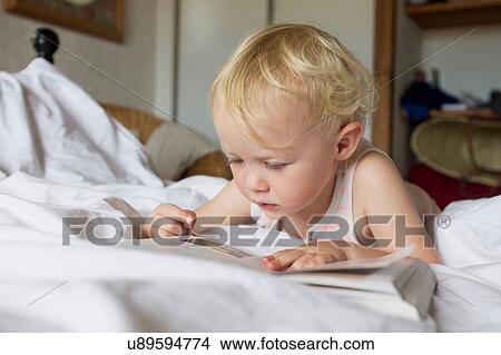 Female toddler lying in bed reading a book View Large Photo Image Picture - Female toddler lying in bed reading a book. Fotosearch