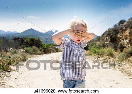 Stock Photo - Female toddler on dirt track with hands covering eyes, Calvi, Corsica, France. Fotosearch