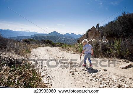 Stock Image - Female toddler on dirt track with walking stick, Calvi, Corsica, France. Fotosearch