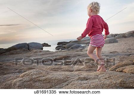 Stock Photography - Female toddler toddling on coastal rock, Calvi, Corsica, France. Fotosearch