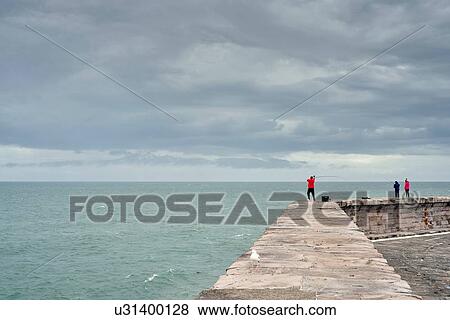 Stock Photo - Fisherman casting from harbour wall, Cumbria, UK. Fotosearch