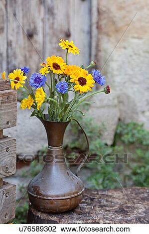 Stock Image - Fresh flowers in metal jug, outdoors. Fotosearch