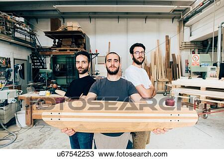 Friends standing in carpentry workshop holding skateboard looking at camera View Large Photo Image Stock Image - Friends standing in carpentry workshop holding skateboard looking at camera. Fotosearch