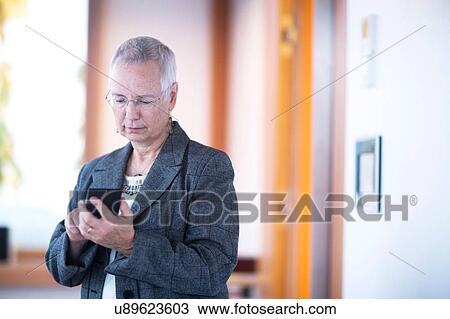Stock Image - Front view of mature woman holding smartphone looking down texting. Fotosearch