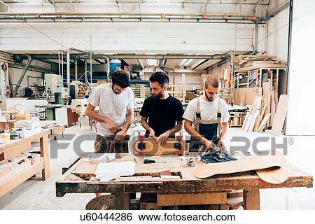 Front view of young men in carpentry workshop standing at workbench attaching wheels to skateboard View Large Photo Image Stock Photograph - Front view of young men in carpentry workshop standing at workbench attaching wheels to skateboard. Fotosearch