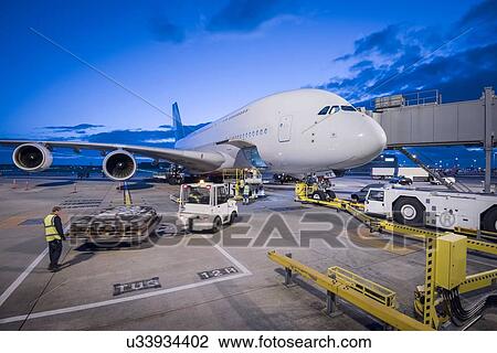 Stock Image - Ground crew attach tug to A380 aircraft on stand at dusk at airport. Fotosearch