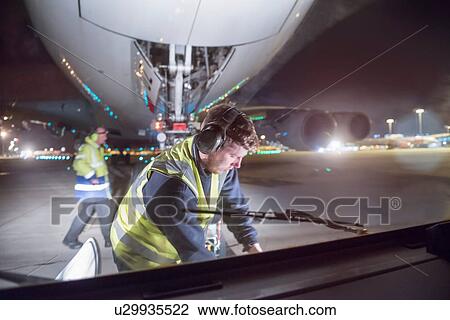 Stock Image - Ground crew uncoupling tug A380 aircraft on runway at night. Fotosearch
