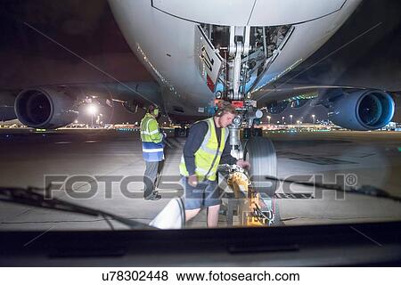 Stock Photo - Ground crew uncoupling tug A380 aircraft on runway at night. Fotosearch