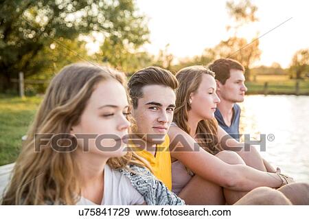 Stock Photo - Group of friends sitting by lake, relaxing. Fotosearch