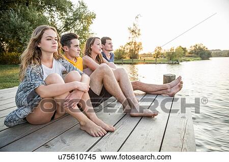Stock Photography - Group of friends sitting on jetty, relaxing. Fotosearch