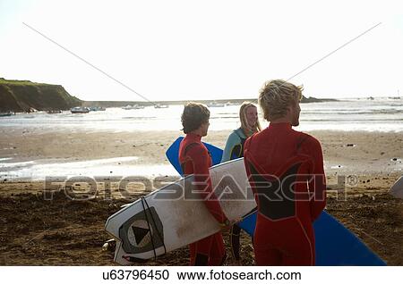 Group of surfers standing on beach, holding surfboards, rear view View Large Photo Image Stock Image - Group of surfers standing on beach, holding surfboards, rear view. Fotosearch