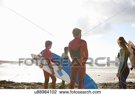 Stock Image - Group of surfers standing on beach, holding surfboards, rear view. Fotosearch
