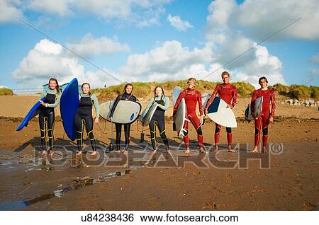 Stock Photograph - Group of surfers, standing on beach, holding surfboards. Fotosearch