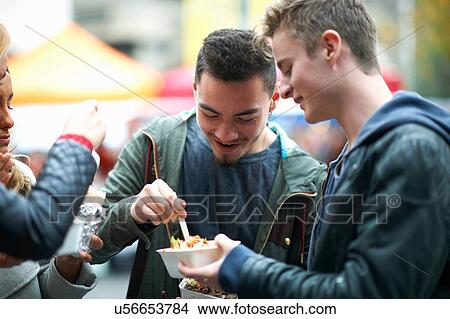 Picture - Group of young adults eating takeaway food, outdoors. Fotosearch