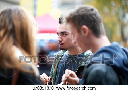 Stock Image - Group of young adults eating takeaway food, outdoors. Fotosearch