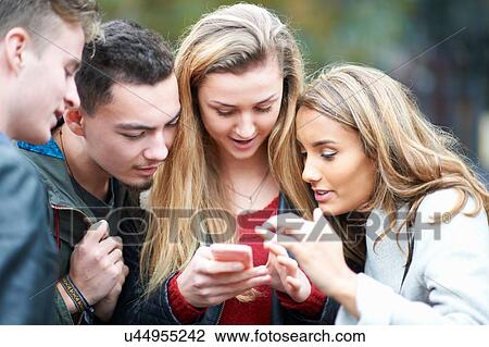 Group of young adults looking at smartphone, outdoors View Large Photo Image Stock Image - Group of young adults looking at smartphone, outdoors. Fotosearch
