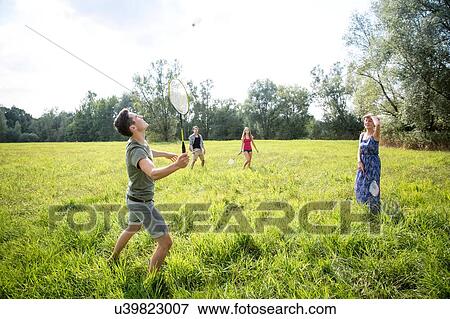 Stock Photo - Group of young adults playing badminton in field. Fotosearch