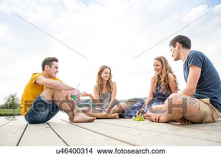 Picture - Group of young adults sitting on jetty, relaxing. Fotosearch