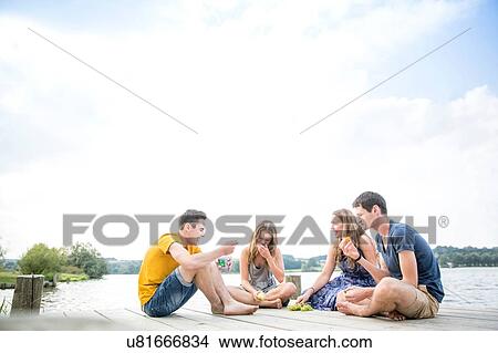 Picture - Group of young adults sitting on jetty, relaxing. Fotosearch