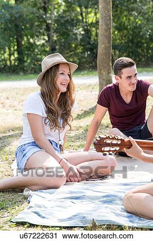 Group of young adults sitting on picnic blanket, young woman playing guitar View Large Photo Image Stock Image - Group of young adults sitting on picnic blanket, young woman playing guitar. Fotosearch