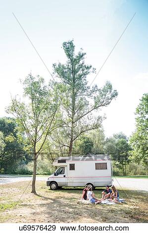 Stock Photo - Group of young adults sitting on picnic blanket, relaxing, camper van in background. Fotosearch