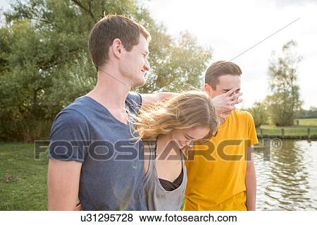 Stock Photo - Group of young adults, standing by lake, fooling around, laughing. Fotosearch