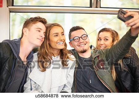 Stock Photo - Group of young friends on train, taking self portrait, using smartphone. Fotosearch