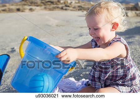 Happy female toddler playing on beach with toy bucket View Large Photo Image Stock Image - Happy female toddler playing on beach with toy bucket. Fotosearch