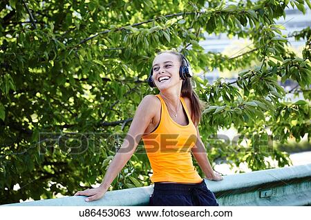 Stock Image - Happy young female runner listening to headphones. Fotosearch