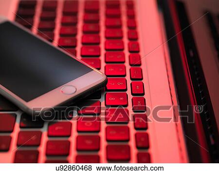 High angle view of cellular phone on computer keyboard in red lighting View Large Photo Image Stock Photo - High angle view of cellular phone on computer keyboard in red lighting. Fotosearch