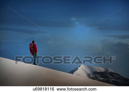 Stock Photograph - Male climber standing on ridge looking out, Canton Bern, Switzerland. Fotosearch
