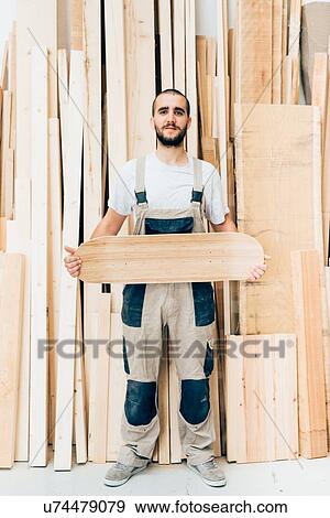 Stock Photo - Man holding skateboard in workshop. Fotosearch