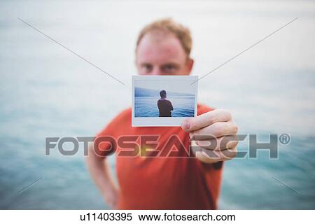 Man holding up photograph of himself by lake View Large Photo Image Stock Photography - Man holding up photograph of himself by lake. Fotosearch