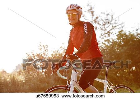Mature cyclist riding past forest View Large Photo Image Stock Image - Mature cyclist riding past forest. Fotosearch