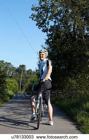 Mature cyclist with bicycle on rural road View Large Photo Image Stock Image - Mature cyclist with bicycle on rural road. Fotosearch