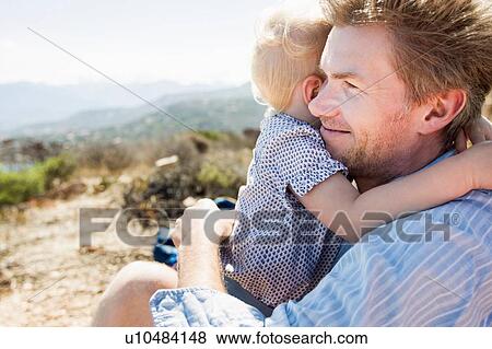 Stock Photo - Mature man and toddler daughter hugging, Calvi, Corsica, France. Fotosearch