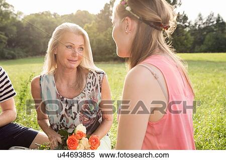 Mature woman holding flowers sitting in field talking to young woman View Large Photo Image Stock Photography - Mature woman holding flowers sitting in field talking to young woman. Fotosearch