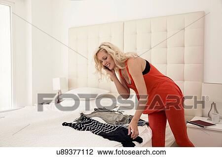 Stock Image - Mature woman in bedroom choosing outfit using smartphone smiling. Fotosearch